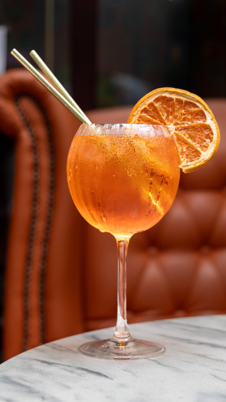 Orange cocktail with slice garnish in wine glass